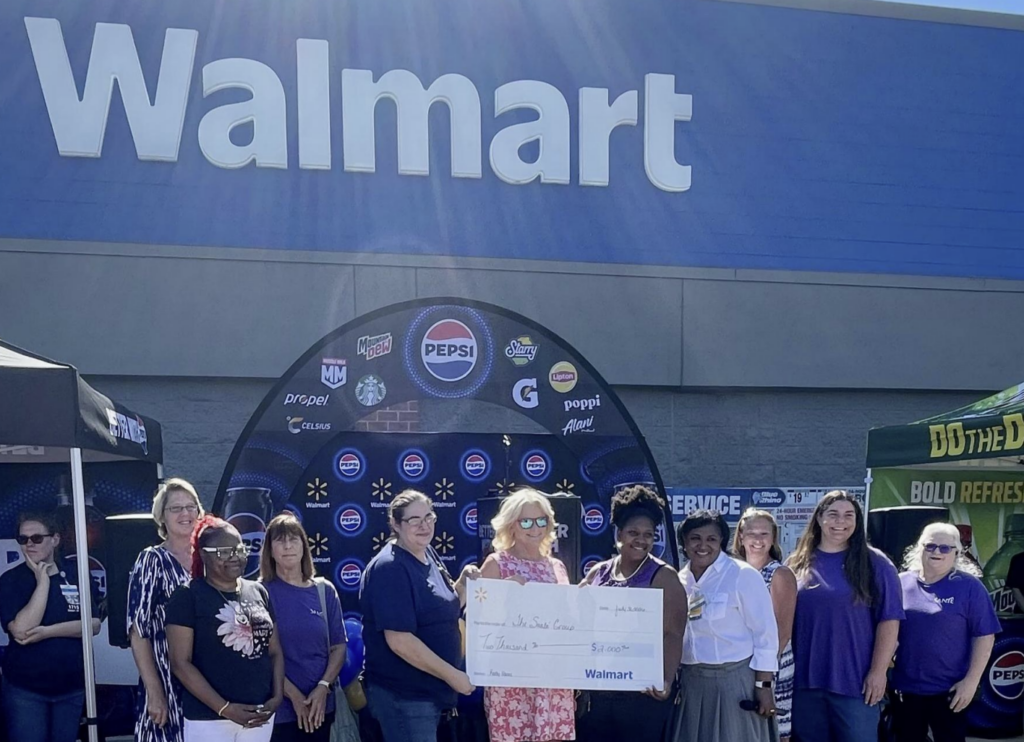 Santé Receives Community Grant from Walmart Easton During Grand Reopening Celebration - Santé Group of diverse adults posing in front of a Walmart store, holding a large ceremonial check at an outdoor event with a branded Pepsi tent behind them.