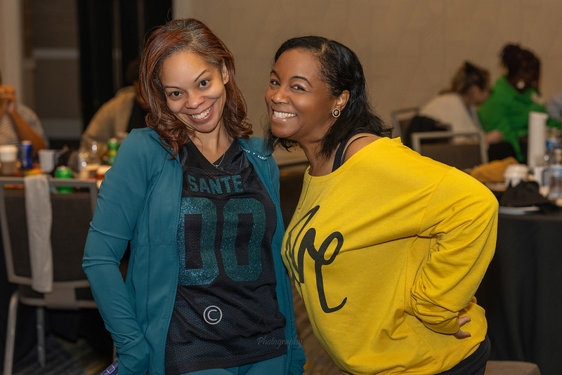You Dont Have to Wait for a Crisis to Ask for Help - Santé Two women smiling and posing together at an indoor event, one in a teal jacket and black shirt, the other in a bright yellow sweater.