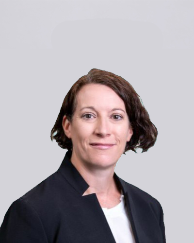 Head-and-shoulders portrait of a smiling woman with short brown hair, wearing a dark blazer against a light gray background.
